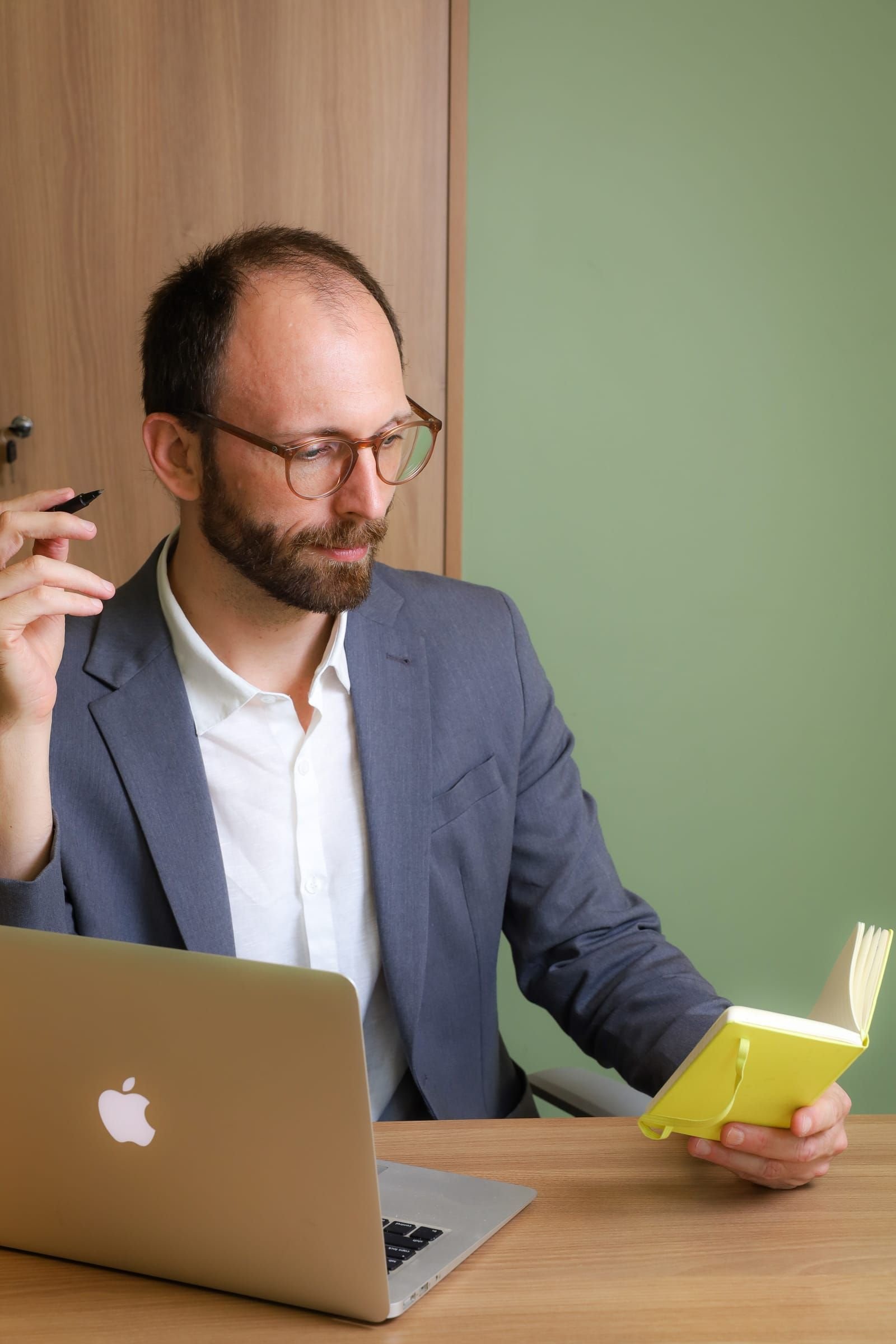 Dr. Roberto Gimena à mesa, segurando um caderno amarelo, ao lado do notebook