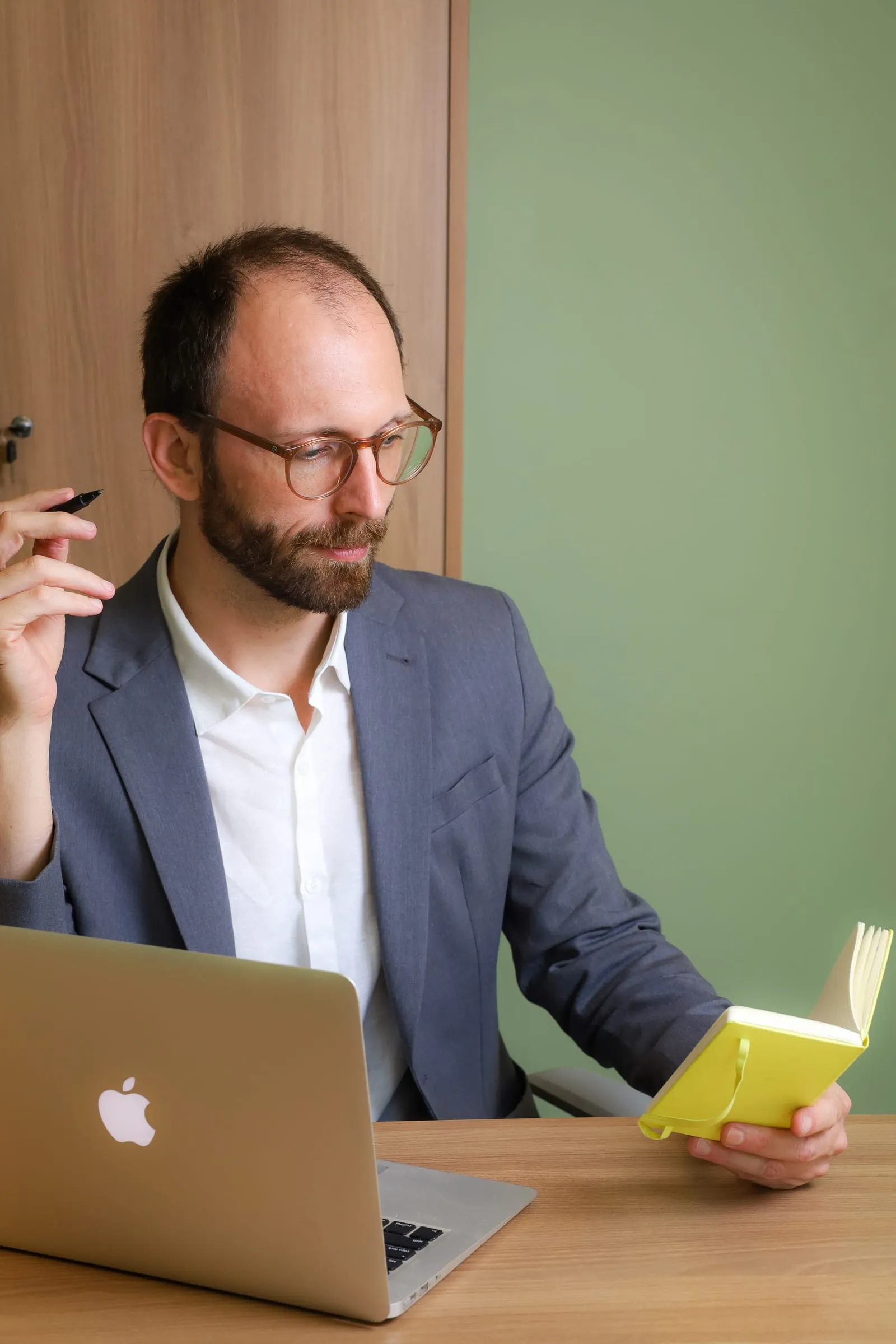 Dr. Roberto Gimena à mesa, segurando um caderno amarelo, ao lado do notebook