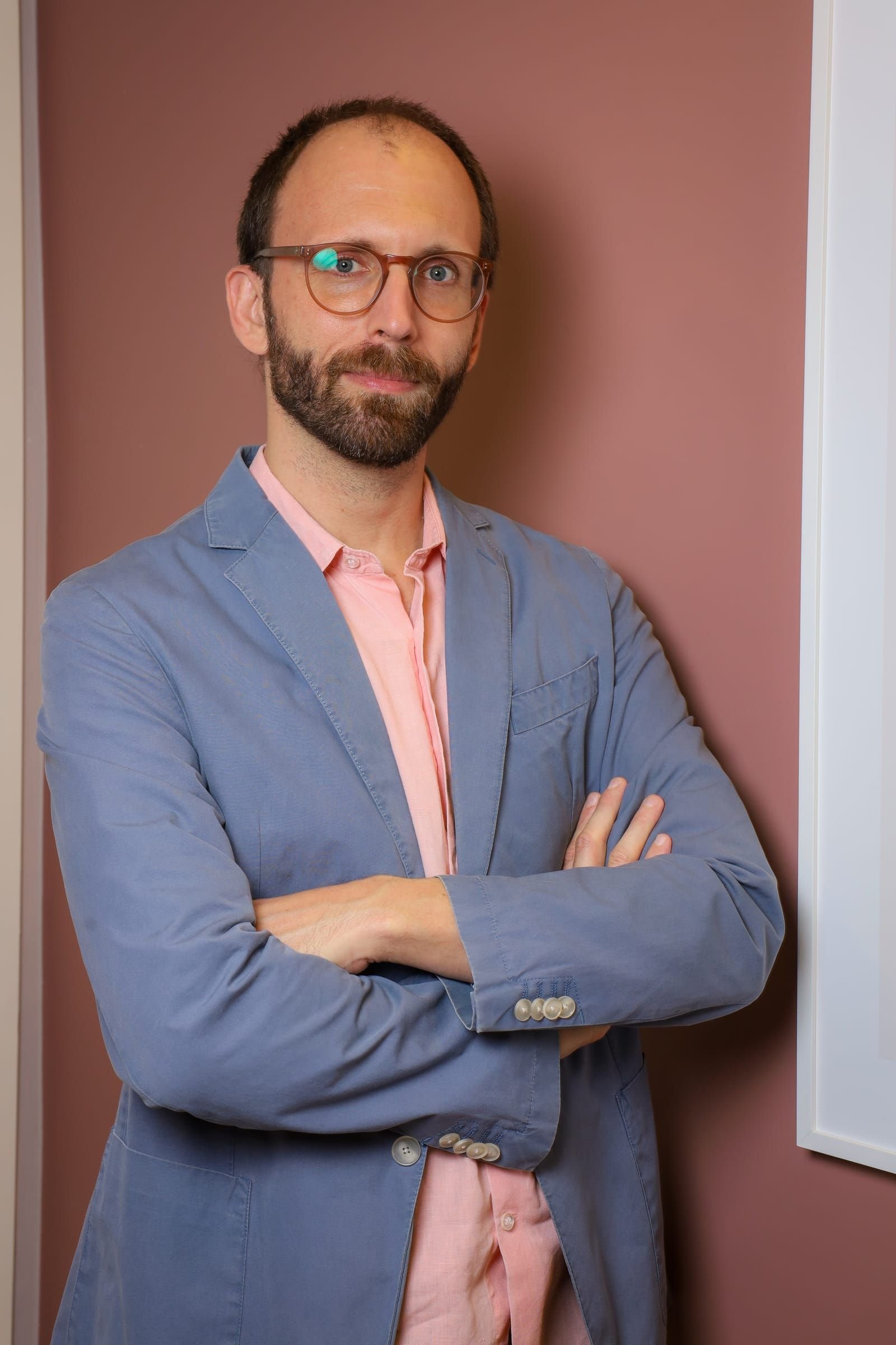 Dr. Roberto Gimena de braços cruzados diante de uma parede rosada no consultório
