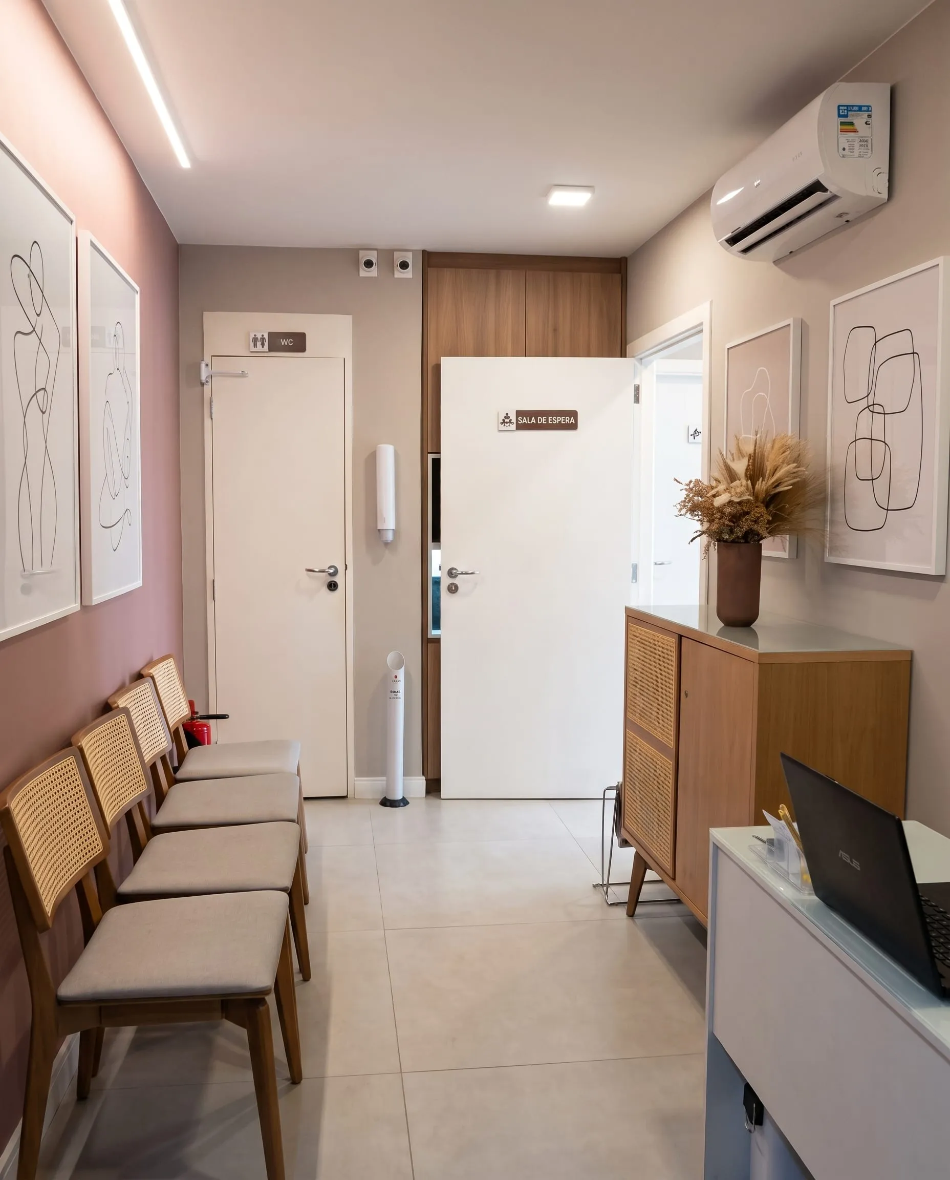 Sala de espera com cadeiras de palhinha, móvel de madeira e quadros